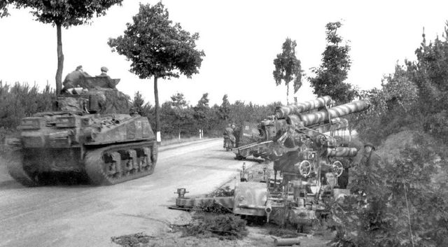 Sherman británico avanzando por una carretera de Bélgica. A la derecha un Flak de 88 mm abandonado por su dotación. 13 de septiembre de 1944
