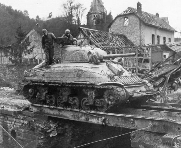 Un Sherman Rhino, corta setos, del 741º Tank Bataillon, cruzando un puente de ingenieros en una aldea alemana. Marzo de 1945